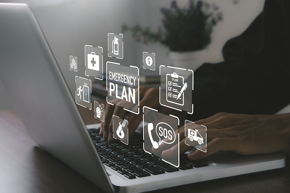 Person typing on a laptop with digital icons floating above the keyboard representing an emergency plan. The icons include first aid, fire extinguisher, exit sign, SOS, and checklist symbols, symbolizing various aspects of emergency preparedness and crisis management.
